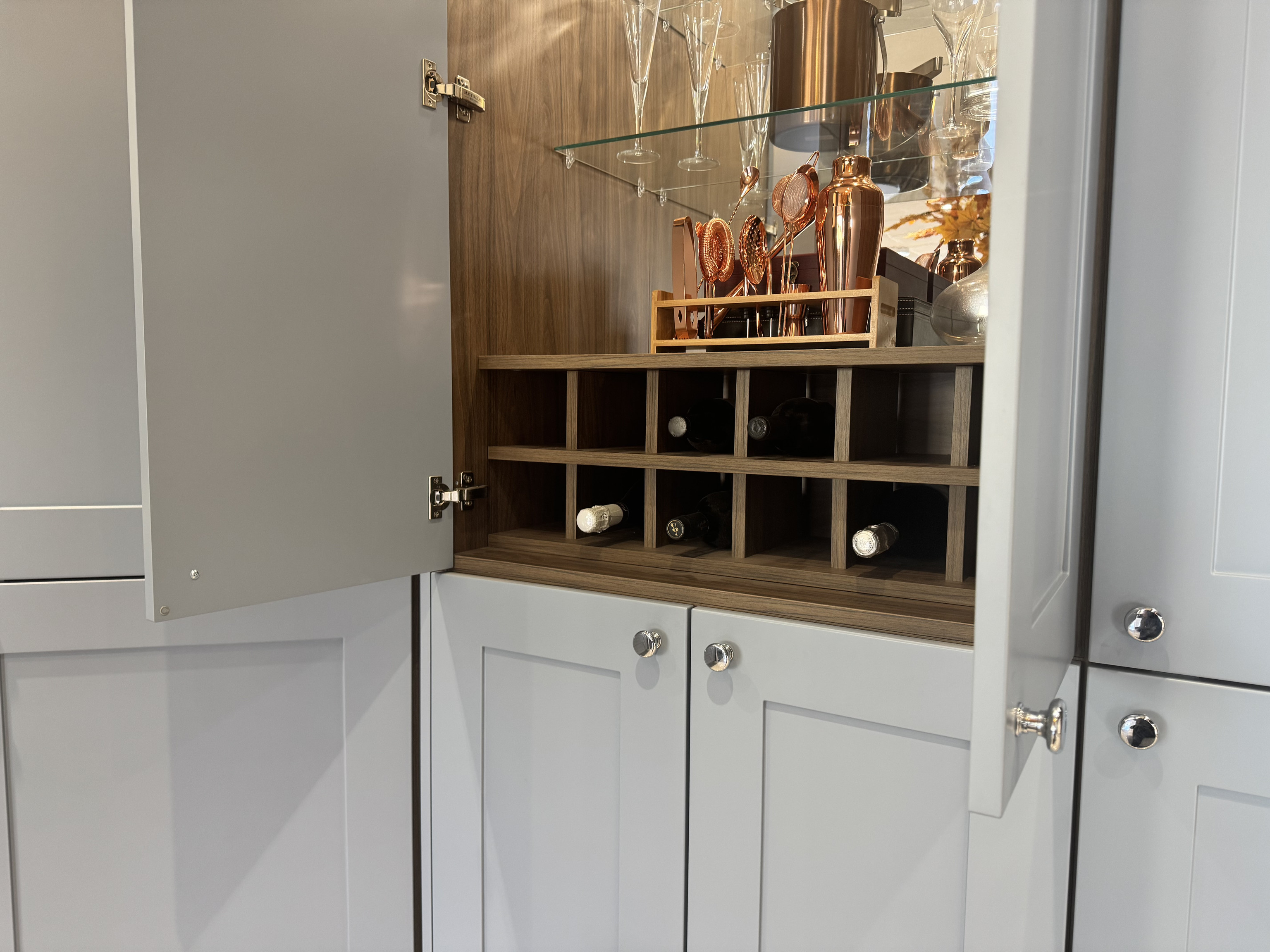 An area within a kitchen cabinet dedicated to storing drinks with mirror and wine rack